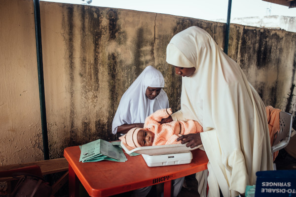 Pengasuh dan bayi di klinik imunisasi — program New Incentives (foto: GiveWell)